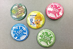缶バッジ5種。二つには「夏まつり」の文字が見え、他の3つは色違いで中央に「15th」とある。
