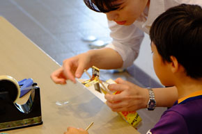 スクリューの付け方を説明しているらしい若い女性と、その手元をのぞき込む幼い男児。