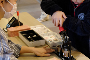 機械のハンドルに力を込める子どもと、機械に手を添える女性。