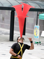 顎にカラーコーンを3個乗せ、それを指さす男性の上半身。