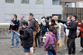建物の屋上でどこかを指さす男性と、同じ方向を向く人々。
