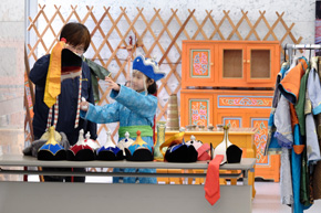 帽子を持つ女性と、それに向かって手を伸ばすモンゴル服姿の女の子。